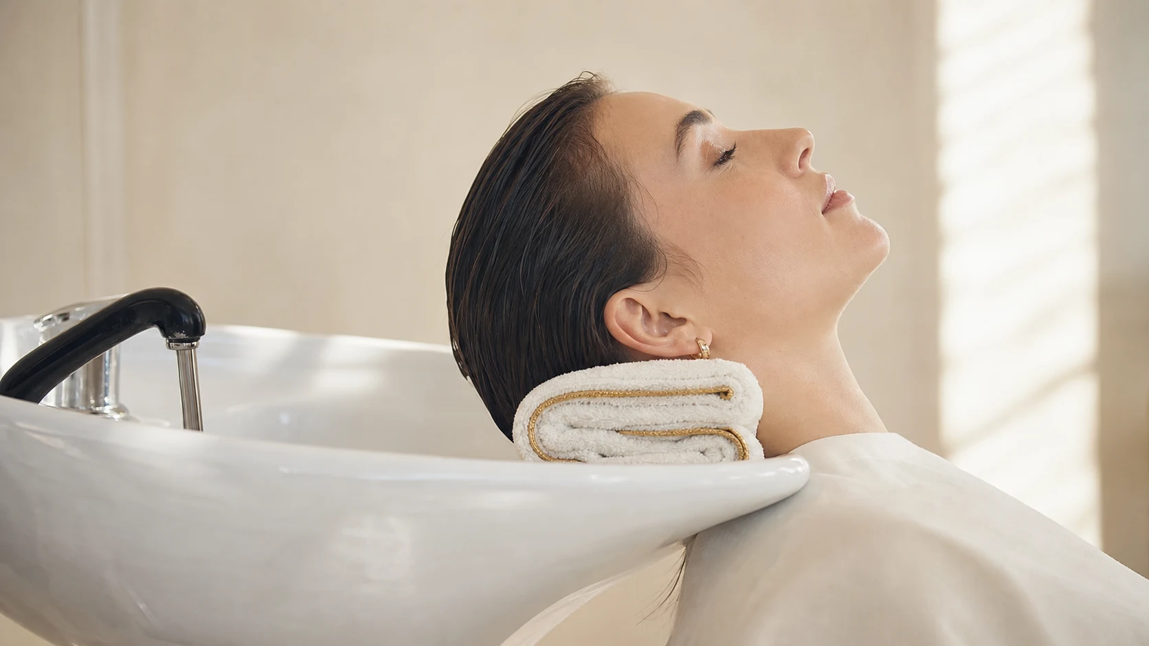 Woman at a salon shampoo basin with a folded towel supporting her neck against hyperextension