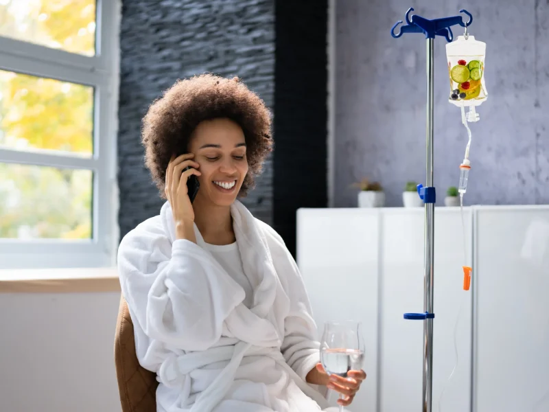 Black Woman receiving IV Therapy with a drink in her hand